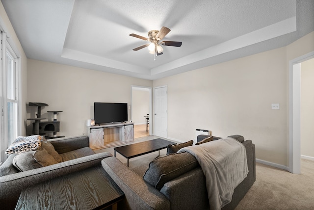 living room featuring light carpet, a textured ceiling, a raised ceiling, and ceiling fan