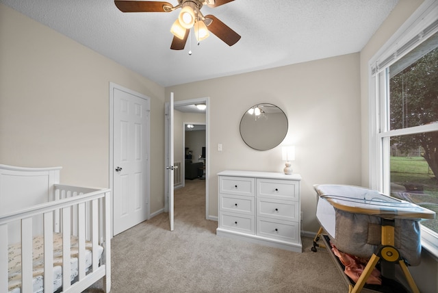 carpeted bedroom featuring ceiling fan, a crib, and a textured ceiling