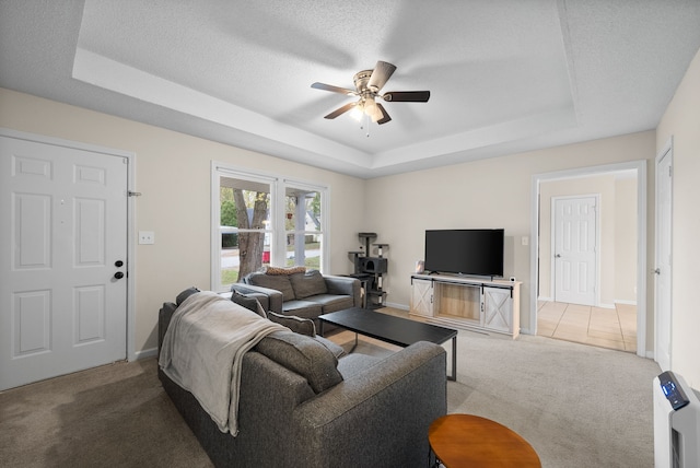 living room with carpet flooring, a textured ceiling, a raised ceiling, and ceiling fan