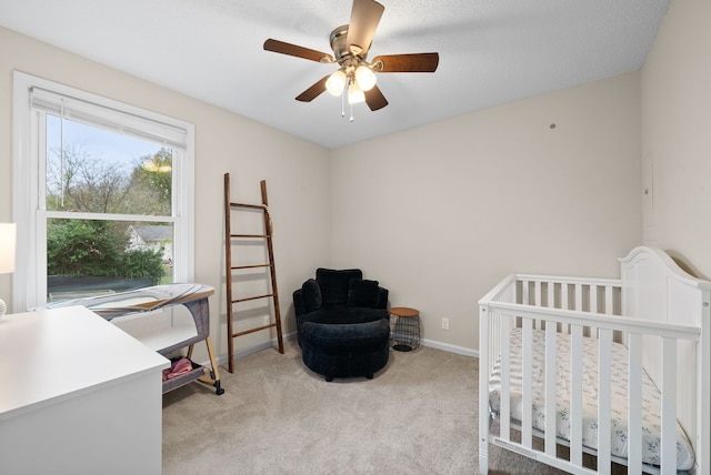 bedroom featuring ceiling fan, a nursery area, a textured ceiling, and light carpet