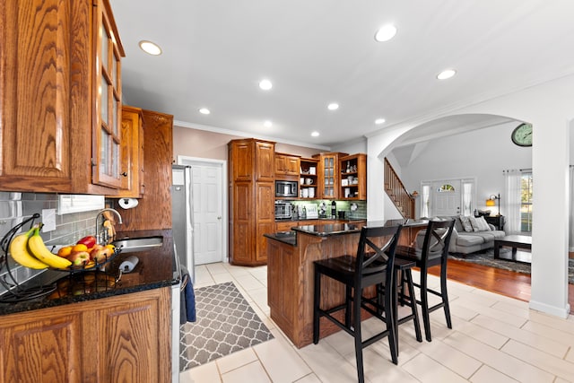 kitchen with sink, stainless steel microwave, backsplash, a breakfast bar, and light tile patterned flooring