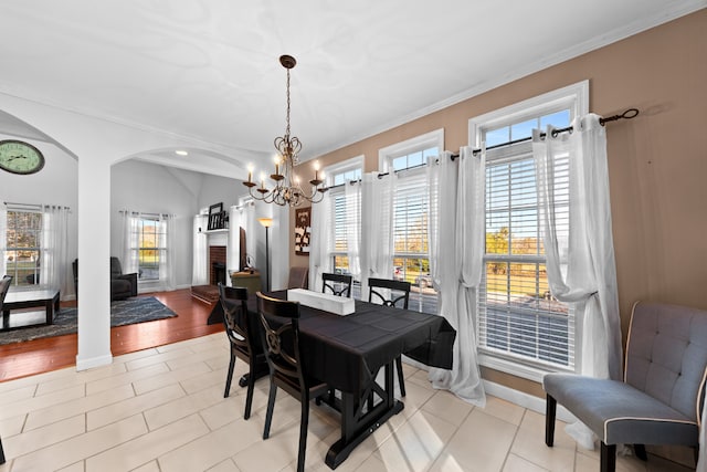 tiled dining space featuring a fireplace, ornamental molding, a chandelier, and a healthy amount of sunlight