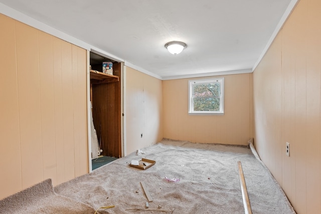 unfurnished bedroom with carpet flooring, a closet, ornamental molding, and wood walls