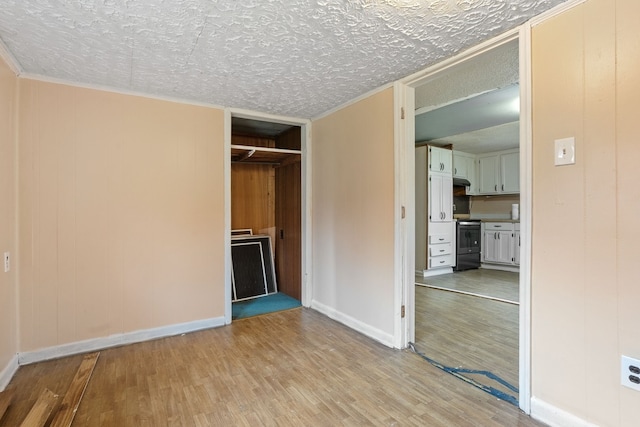 unfurnished bedroom featuring wood walls, crown molding, light hardwood / wood-style flooring, a textured ceiling, and a closet