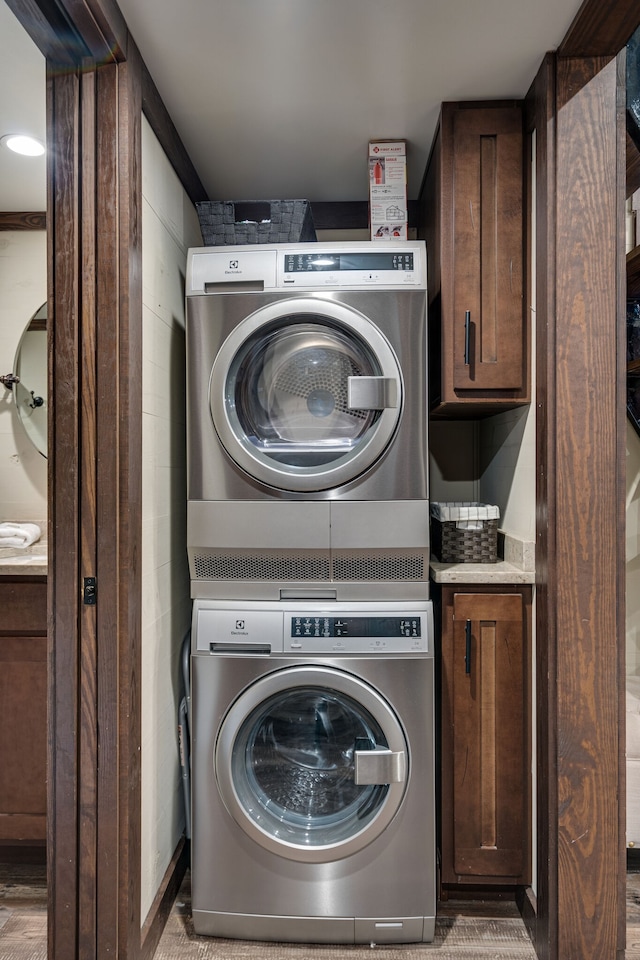 clothes washing area with cabinets, light hardwood / wood-style flooring, and stacked washer and clothes dryer