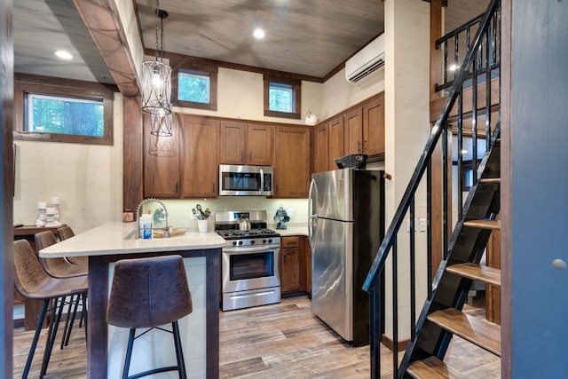 kitchen with a kitchen bar, stainless steel appliances, a wall mounted AC, decorative light fixtures, and light hardwood / wood-style flooring