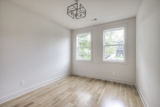 unfurnished room featuring a chandelier and light hardwood / wood-style flooring