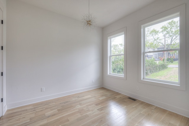 unfurnished room with a wealth of natural light, light wood-type flooring, and an inviting chandelier