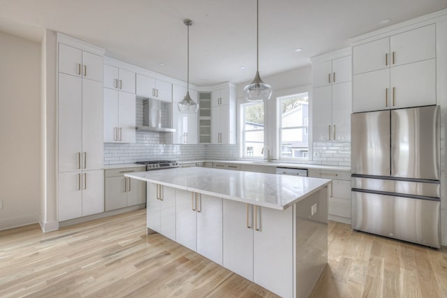 kitchen with white cabinets, appliances with stainless steel finishes, a kitchen island, and wall chimney range hood