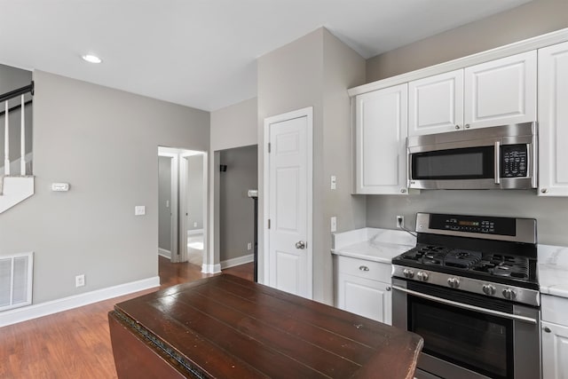 kitchen featuring white cabinetry, stainless steel appliances, light stone counters, and wood-type flooring