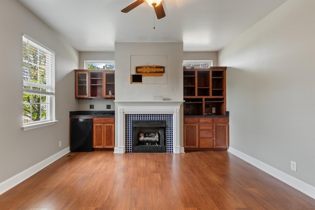 unfurnished living room featuring ceiling fan, wood-type flooring, and a tile fireplace