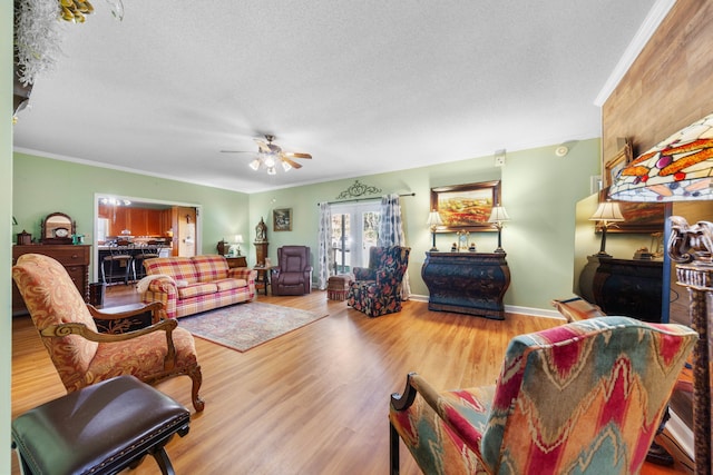 living room with wood-type flooring, a textured ceiling, ceiling fan, and ornamental molding