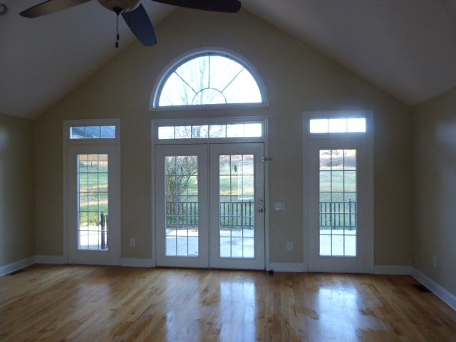 doorway with light hardwood / wood-style floors, high vaulted ceiling, and ceiling fan