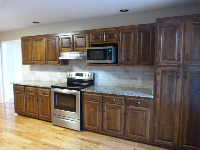 kitchen featuring light stone countertops, appliances with stainless steel finishes, light wood-type flooring, and decorative backsplash