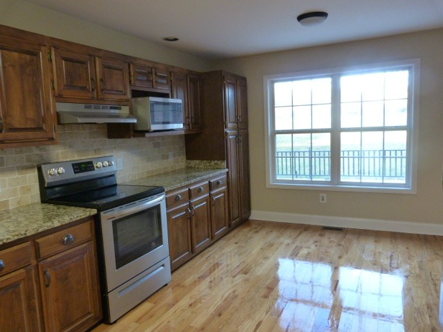 kitchen with decorative backsplash, light stone countertops, stainless steel appliances, and light hardwood / wood-style flooring