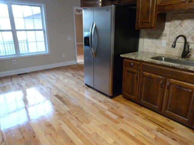 kitchen with sink, stainless steel fridge with ice dispenser, light stone counters, backsplash, and light hardwood / wood-style floors