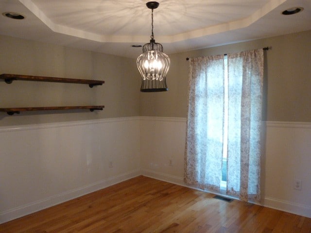 empty room featuring a tray ceiling, a notable chandelier, and hardwood / wood-style flooring