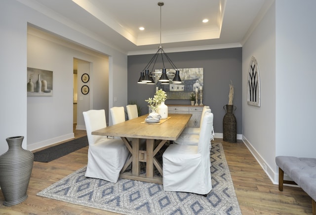 dining room featuring crown molding, a raised ceiling, and light wood-type flooring