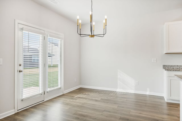 unfurnished dining area featuring a healthy amount of sunlight, light wood-type flooring, and an inviting chandelier