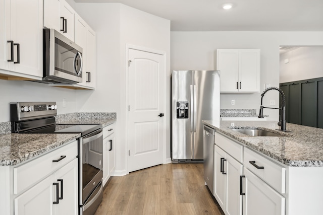 kitchen with sink, light hardwood / wood-style flooring, light stone countertops, white cabinetry, and stainless steel appliances