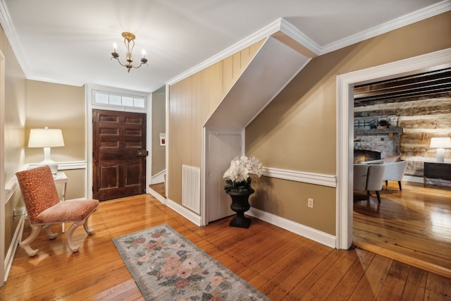 foyer featuring a stone fireplace, crown molding, light hardwood / wood-style floors, and an inviting chandelier