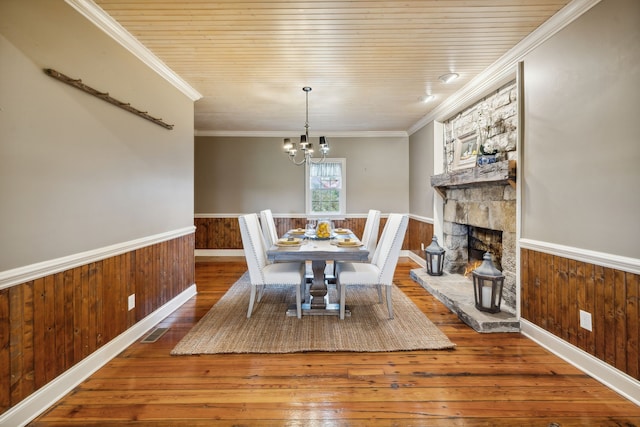 dining space featuring wooden walls, hardwood / wood-style flooring, a stone fireplace, and ornamental molding