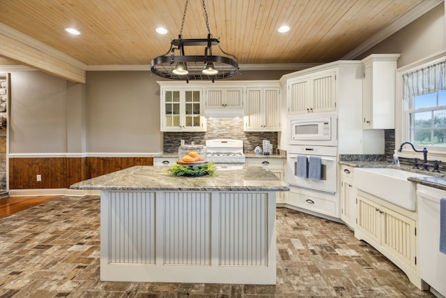 kitchen featuring light stone countertops, white appliances, a kitchen island, hanging light fixtures, and wood walls