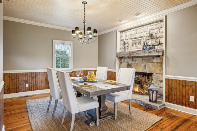 dining area featuring wood walls, a fireplace, ornamental molding, and hardwood / wood-style flooring