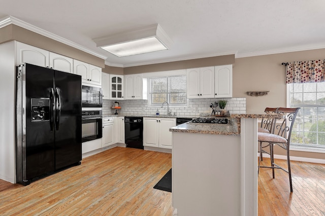 kitchen featuring kitchen peninsula, white cabinetry, a breakfast bar, and black appliances