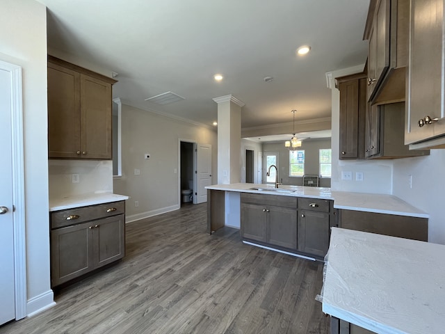 kitchen featuring sink, dark wood-type flooring, kitchen peninsula, crown molding, and decorative light fixtures