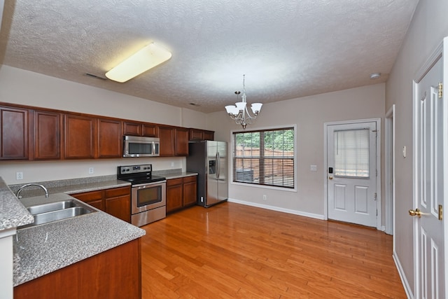 kitchen featuring stainless steel appliances, sink, pendant lighting, an inviting chandelier, and light hardwood / wood-style flooring