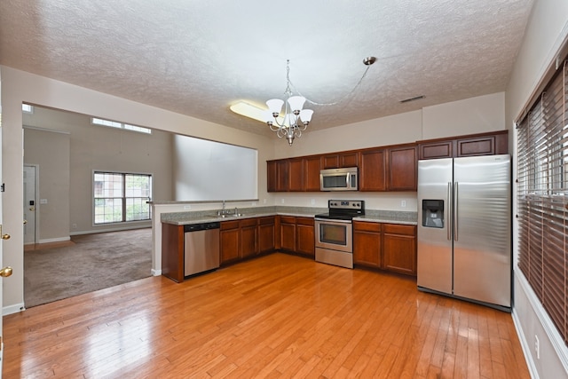 kitchen with light wood-type flooring, a textured ceiling, stainless steel appliances, an inviting chandelier, and hanging light fixtures