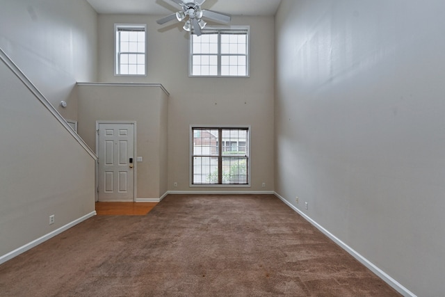 carpeted foyer featuring ceiling fan, a healthy amount of sunlight, and a towering ceiling