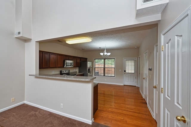 kitchen with an inviting chandelier, dark hardwood / wood-style flooring, kitchen peninsula, pendant lighting, and appliances with stainless steel finishes