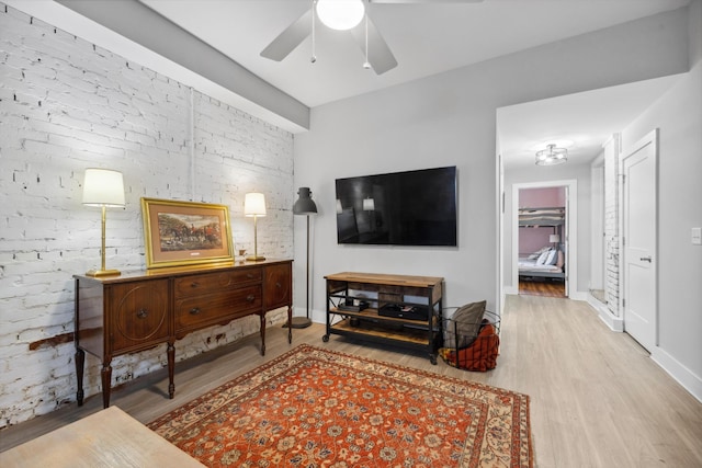 living room with ceiling fan, light hardwood / wood-style floors, and brick wall