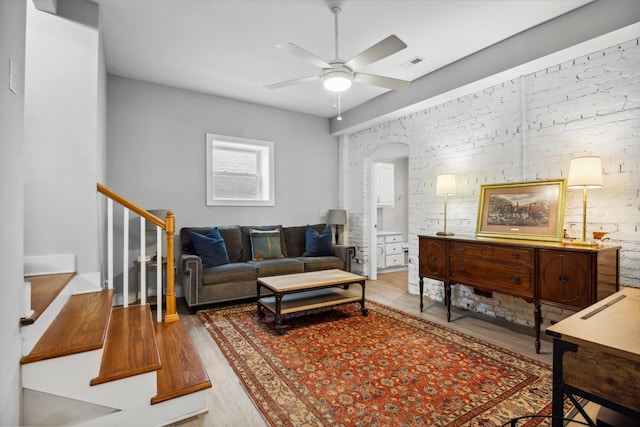 living room featuring wood-type flooring, ceiling fan, and brick wall