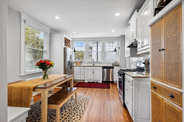 kitchen featuring sink, stainless steel appliances, light stone counters, light hardwood / wood-style flooring, and white cabinets