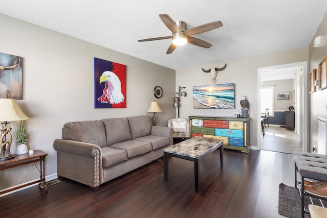 living room featuring ceiling fan, dark wood-type flooring, and a textured ceiling