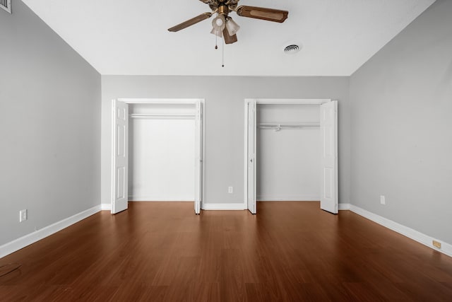 unfurnished bedroom with ceiling fan, dark wood-type flooring, and two closets