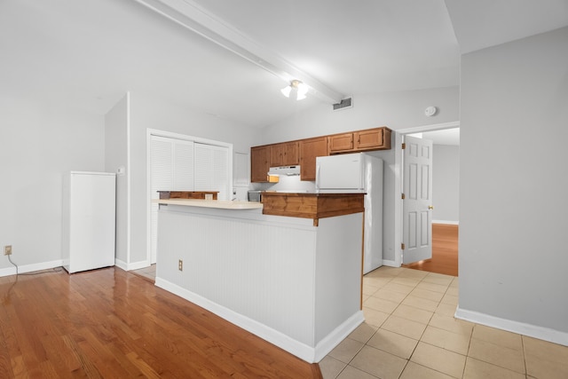 kitchen with vaulted ceiling with beams, white fridge, light hardwood / wood-style floors, and kitchen peninsula