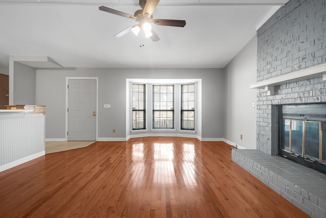 unfurnished living room with ceiling fan, wood-type flooring, and a brick fireplace