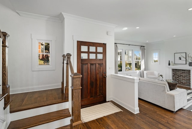 foyer entrance with a brick fireplace, dark wood-type flooring, and ornamental molding