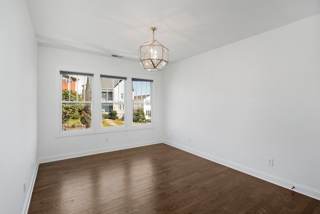 empty room with dark hardwood / wood-style flooring and an inviting chandelier