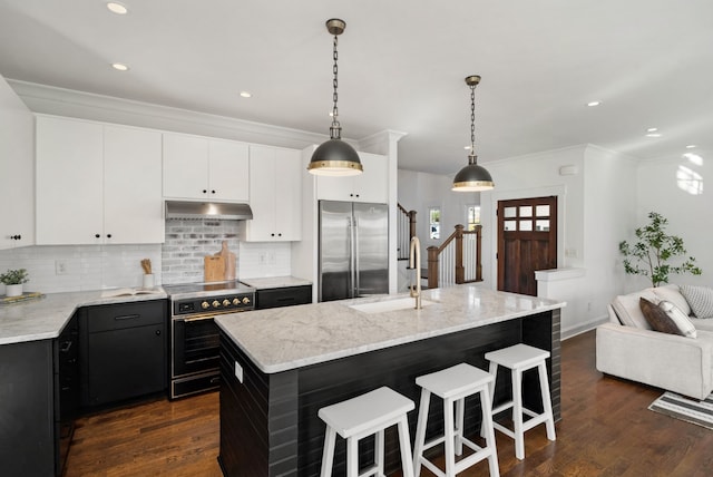 kitchen with hanging light fixtures, stainless steel appliances, dark hardwood / wood-style flooring, backsplash, and an island with sink