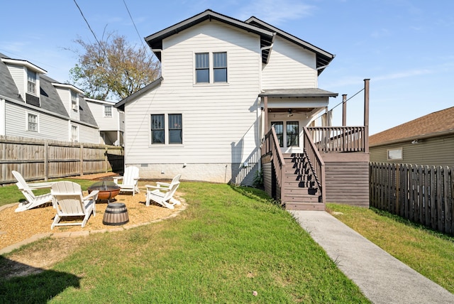 back of house featuring a fire pit, a deck, and a lawn