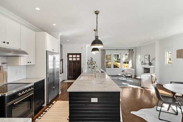 kitchen with stainless steel fridge, electric range oven, decorative light fixtures, white cabinetry, and an island with sink