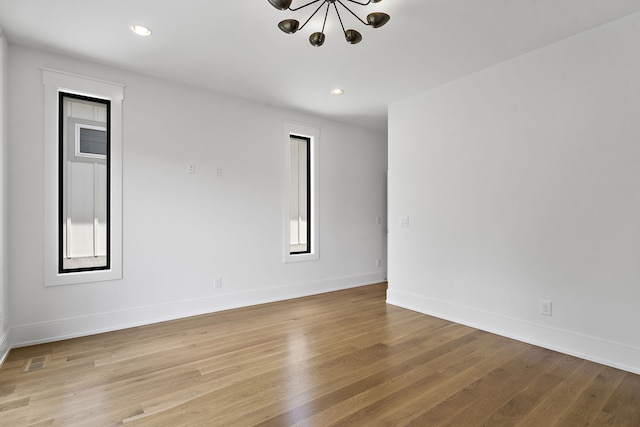 unfurnished room with plenty of natural light, a notable chandelier, and light hardwood / wood-style flooring