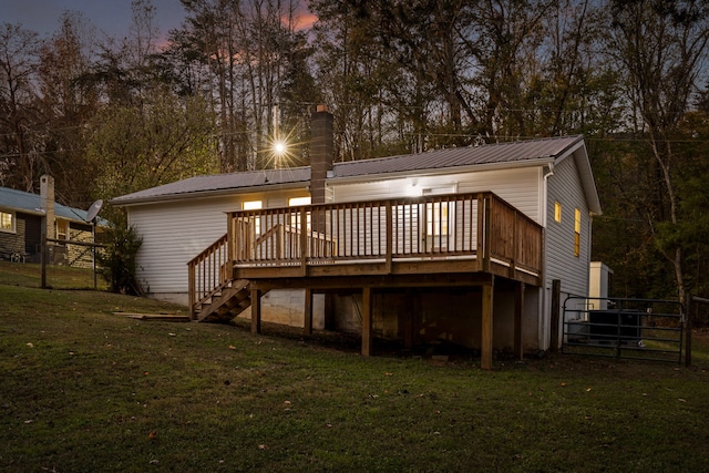 back house at dusk with a deck and a lawn