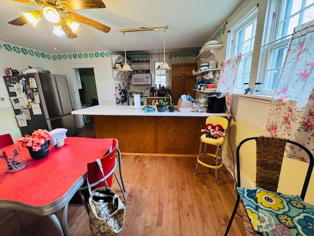 kitchen featuring kitchen peninsula, stainless steel fridge, ceiling fan, pendant lighting, and light hardwood / wood-style flooring