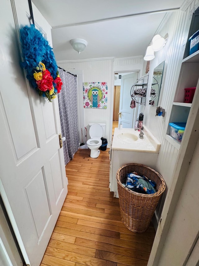 bathroom featuring vanity, wooden walls, hardwood / wood-style flooring, toilet, and curtained shower